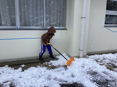 ショベルで雪かきをする児童