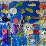 昇降口の壁面飾り。子どもたちが作った魚、亀、クラゲなどが青く塗られた模造紙に貼られています。