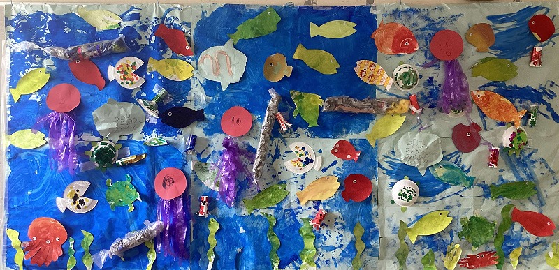 昇降口の壁面飾り。子どもたちが作った魚、亀、クラゲなどが青く塗られた模造紙に貼られています。